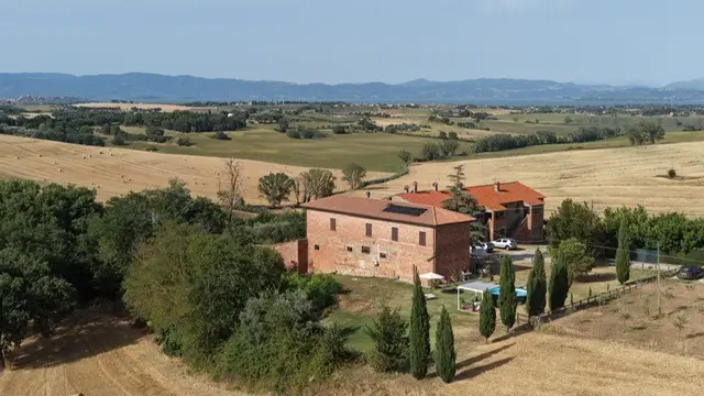 Drone-foto van Toscaanse bakstenen boerderij met zwembad en cipressenlaan, omringd door akkers en een meer in de verte